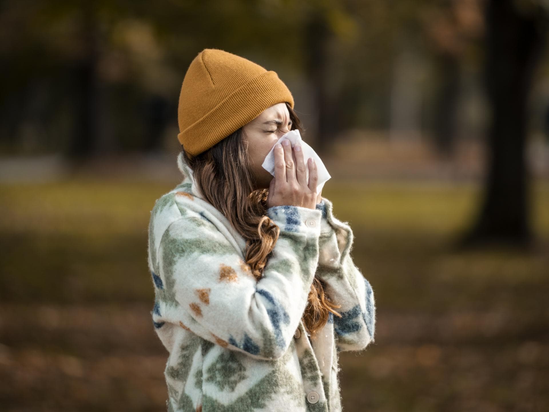 Erkältung oder nur eine Allergie? Frau mit brauner Mütze schnaubt sich die Nase im Freien