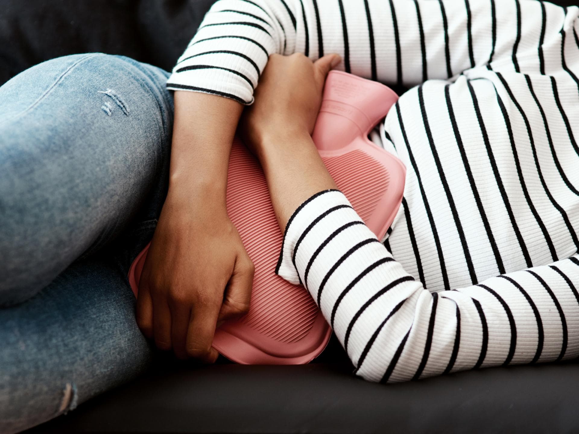 Frau liegt mit Wärmflasche auf dem Bauch auf dem Sofa Frau liegt mit Wärmflasche auf dem Bauch auf dem Sofa