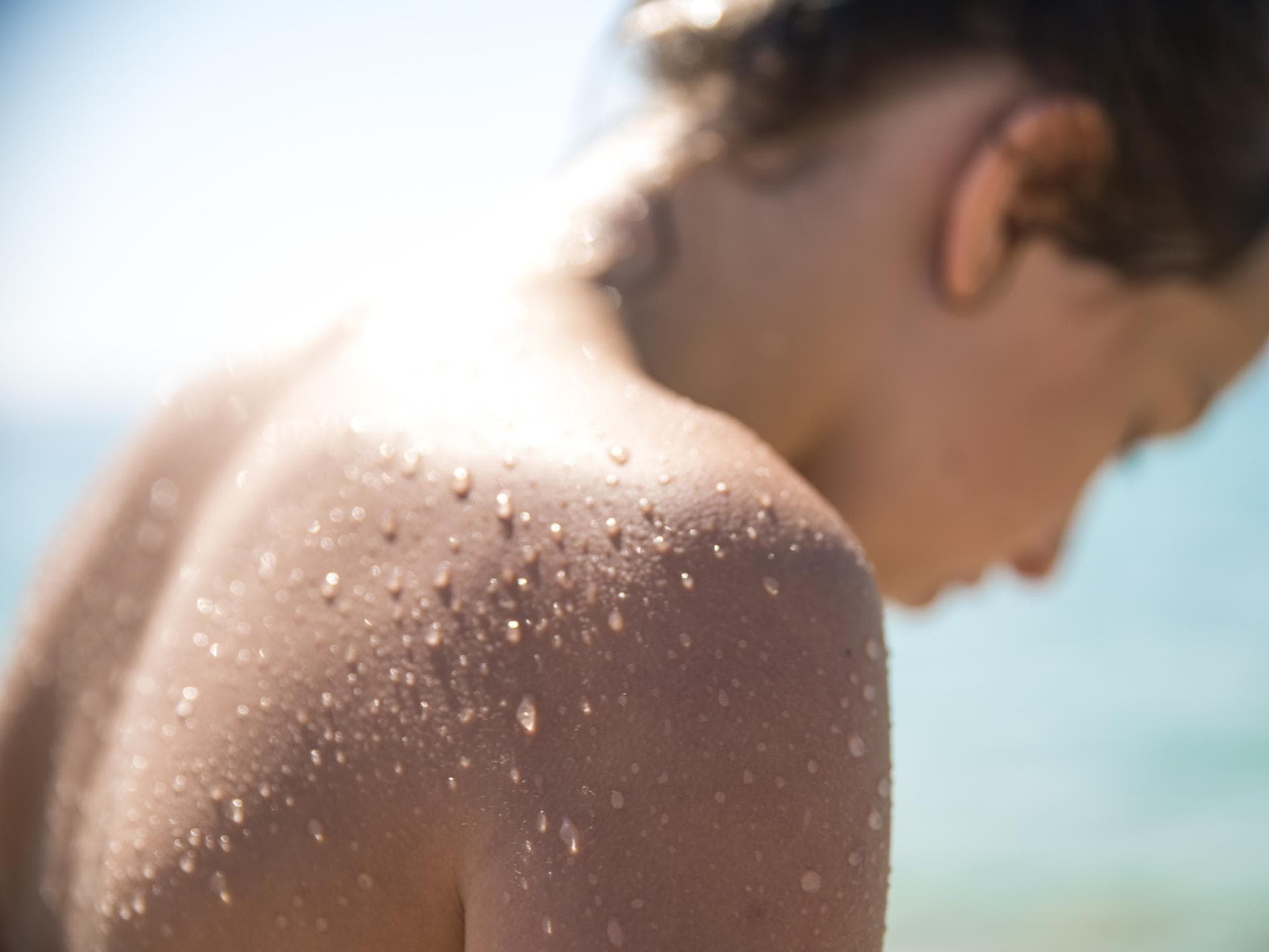 Gesunde Haut Eine Junge Frau, die sich im Sommer am Wasser befindet und deren Rücken mit Wasserperlen überzogen ist