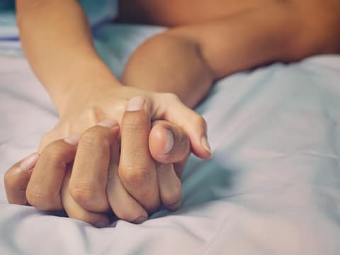 Zwei ineinander verwobene Hände im Bett Zwei ineinander verwobene Hände im Bett