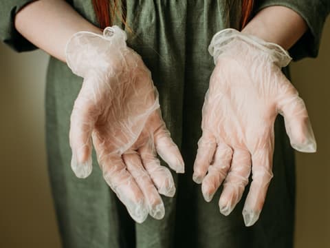 Welche Symptome gibt es bei einer Latexallergie? Ärztin hält in Latexhandschuhe verpackte Hände mit den Handflächen nach vorn in die Kamera