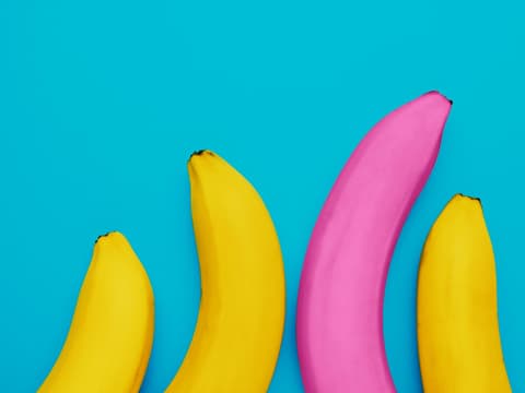 Was bedeutet ein blauer Fleck am Penis? Eine lange pinke Banane neben drei kleineren gelben Bananen als Symbol für unterschiedliche Penislängen