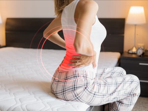 Frau sitzt auf dem Bett und hat Rückenschmerzen Frau sitzt auf dem Bett und hat Rückenschmerzen