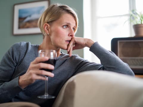Nachdenkliche Frau sitzt auf dem Sofa mit einem Glas Wein in der Hand Nachdenkliche Frau sitzt auf dem Sofa mit einem Glas Wein in der Hand