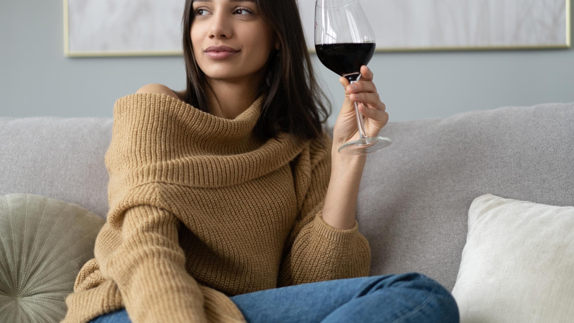 Frau sitzt mit einem Glas Rotwein auf dem Sofa Frau sitzt mit einem Glas Rotwein auf dem Sofa