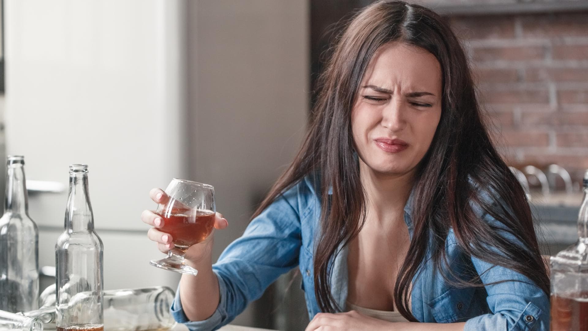 Frau mit dunklen Haaren verzieht das Gesicht Frau verzieht das Gesicht und hält ein Glas in der Hand
